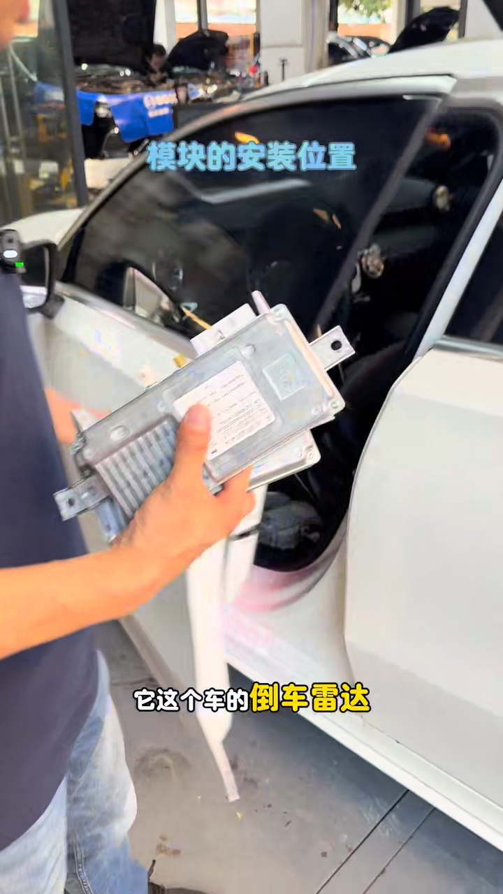 Removed metal-cased reverse-camera control module held beside the Mercedes A200.