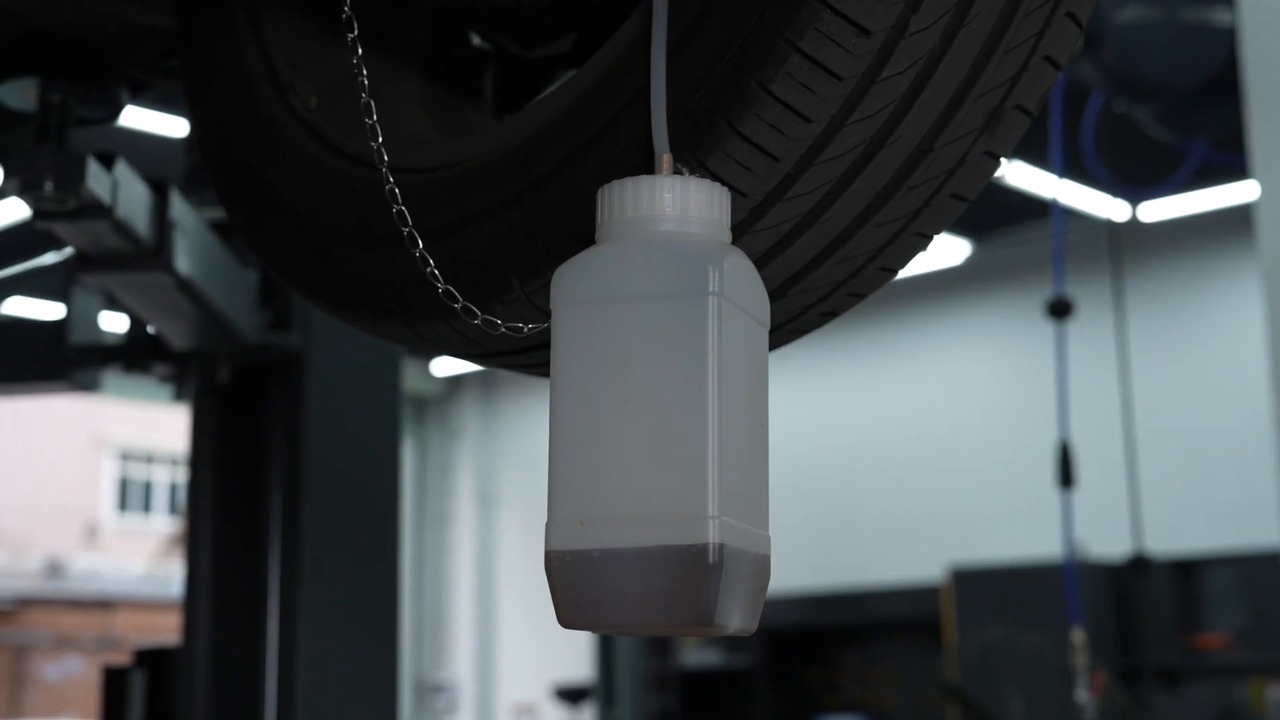 Clear hose and stable used-fluid bottle connected at one wheel service point during an AUTOOL AST612 workflow.