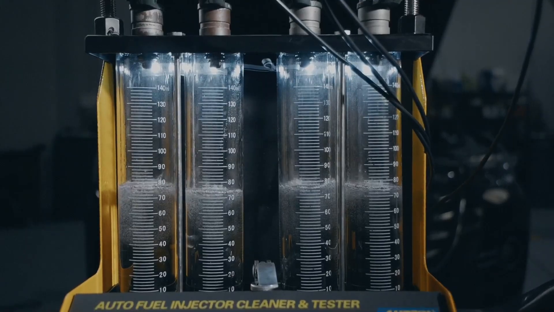 Four graduated AUTOOL CT150 measuring tubes collecting fluid during a visible injector test.