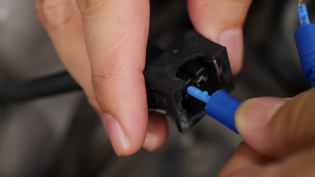 Hands aligning a blue automotive terminal lead with a black connector shell.