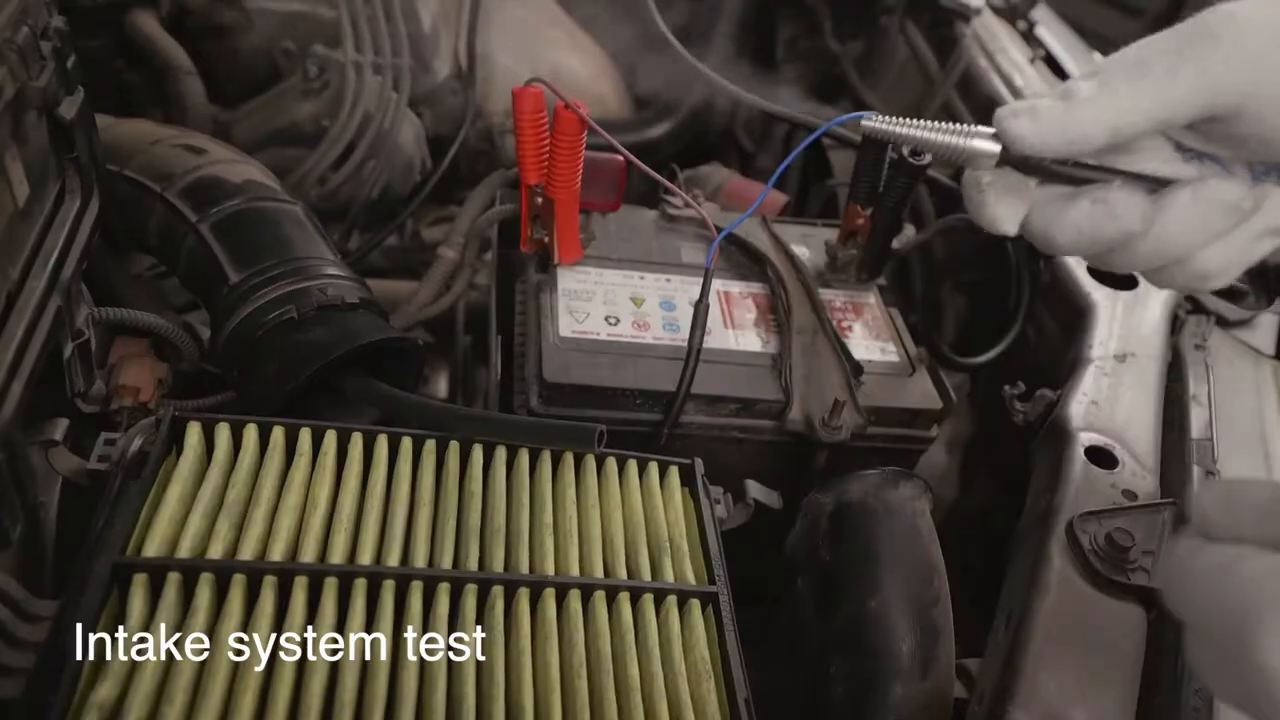 Technician working at the intake while an AUTOOL SDT205 smoke machine is connected in the engine bay.