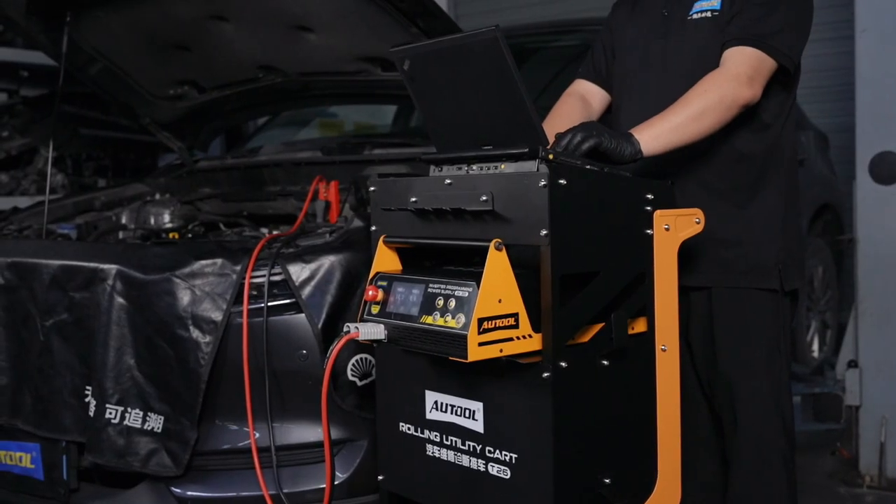 AUTOOL T26 workshop cart parked beside a vehicle with drawers closed and diagnostic battery-test leads contained at the work area.