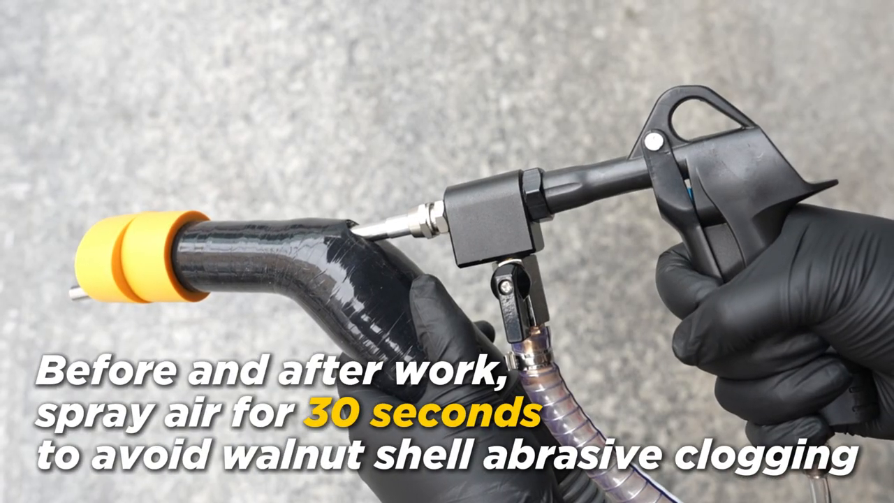 Gloved hands holding a walnut-blasting gun and adapter while air clears the media path.