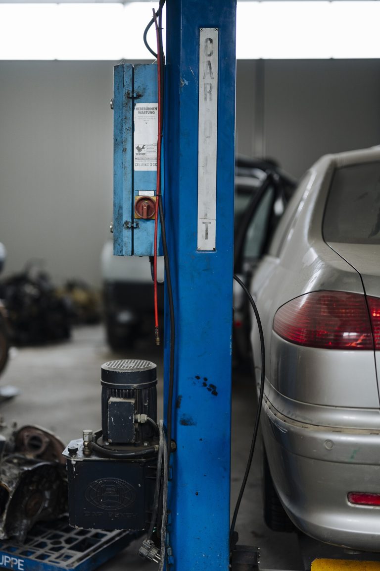 Car positioned beside a blue vehicle lift in a repair shop
