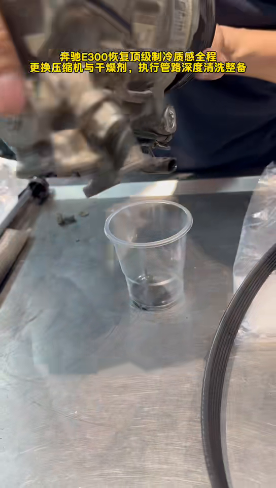 Dark oil draining from the removed Mercedes E300 A/C compressor into a clear cup.