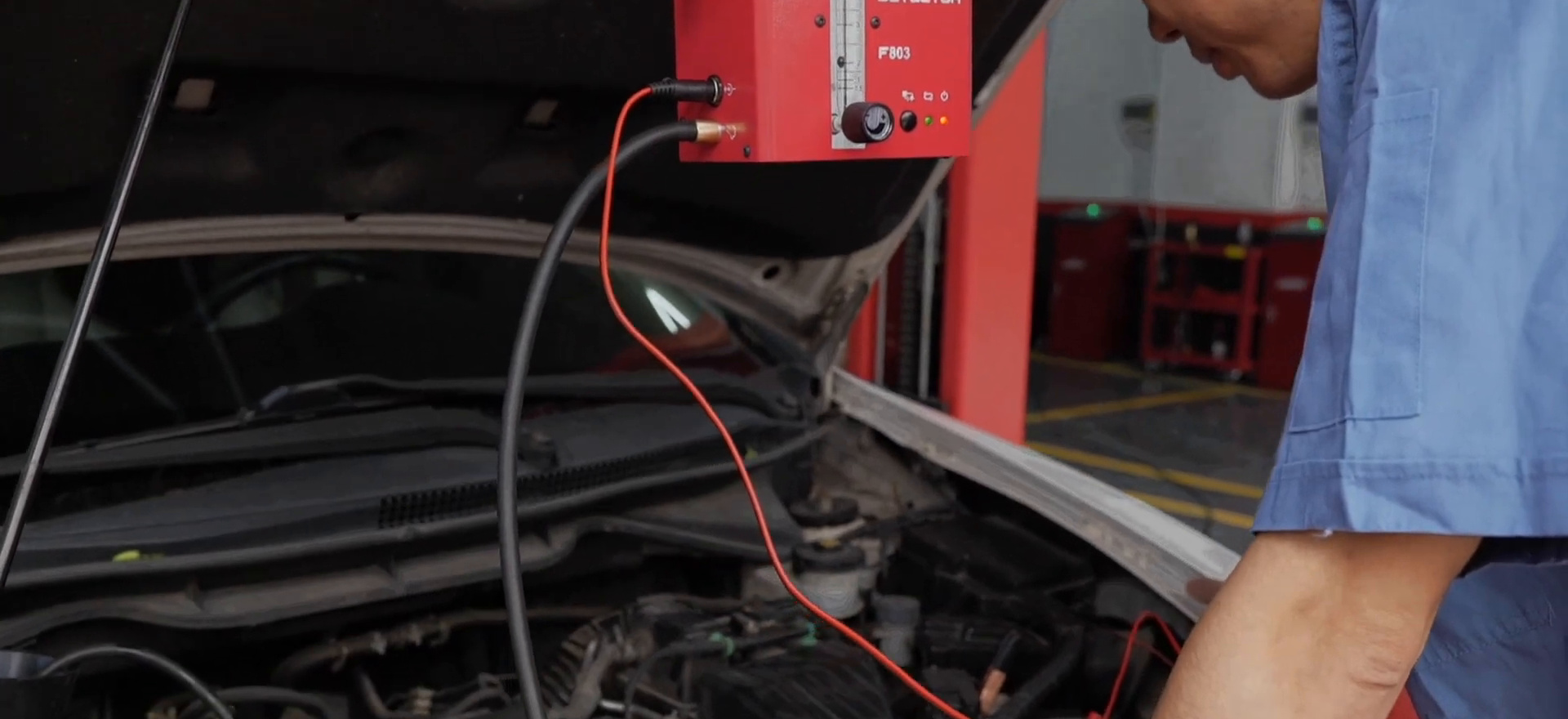 Technician inspecting an engine-bay test path while an FXTUL F803 hangs upright