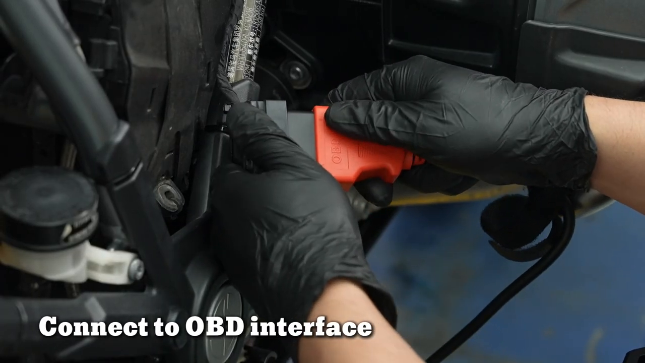 Gloved technician seating a red FXTUL M7 diagnostic adapter at a motorcycle diagnostic interface.