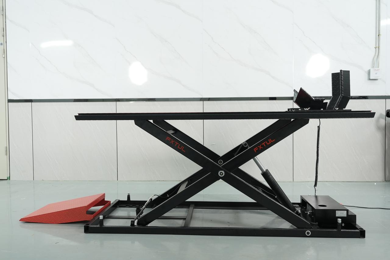 FXTUL TLM-family black motorcycle lift in a raised position with its platform X-frame approach ramp and front wheel restraint visible.