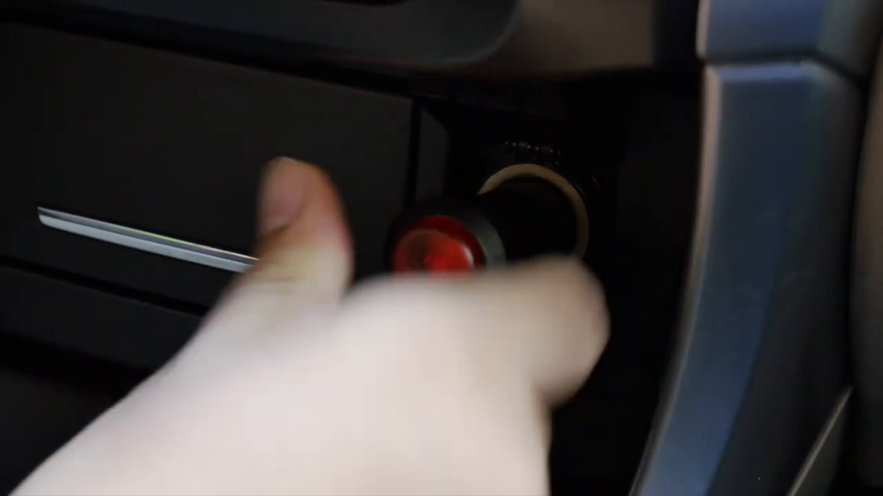 Official M85 video frame showing the supplied car charger being connected to the vehicle accessory socket.