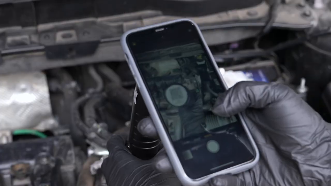 Technician connecting the MRCARTOOL N100 handle to a phone display beside an open engine bay.