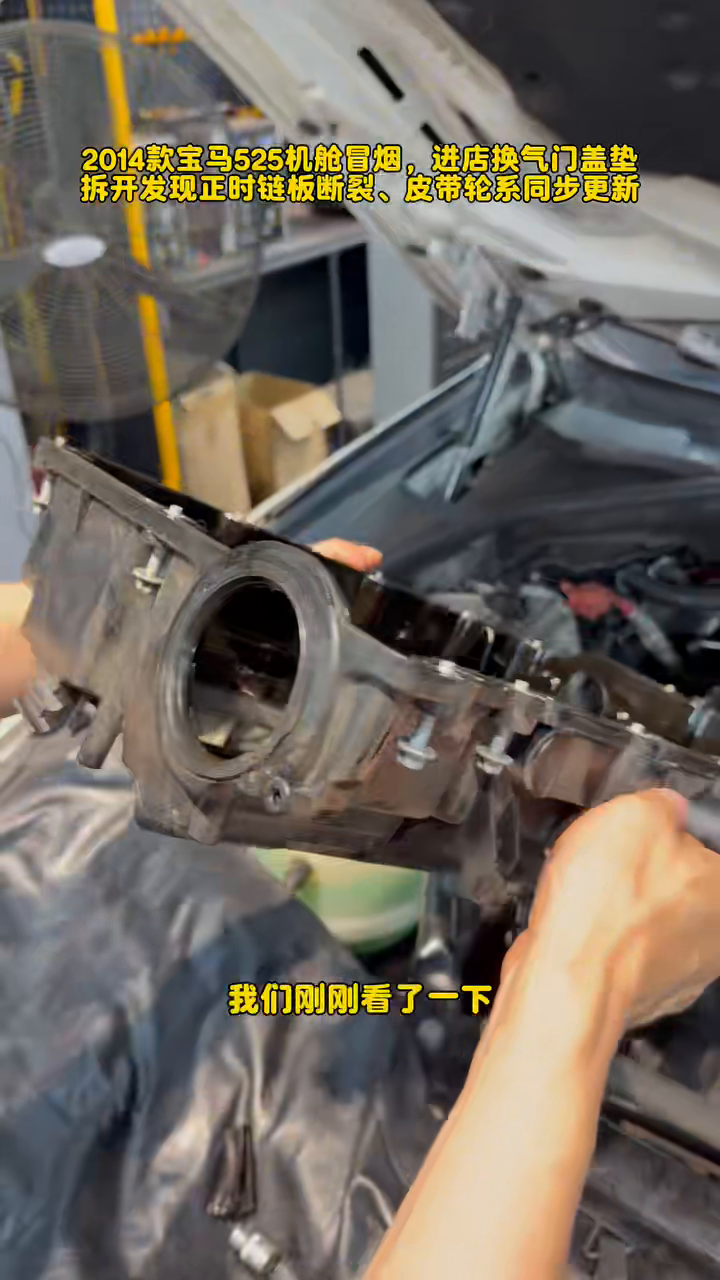 Removed BMW N20 valve cover held above the open engine bay.