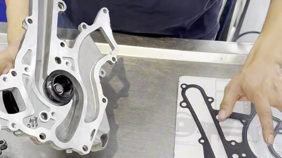 Replacement water pump beside its separate gasket on a workbench.